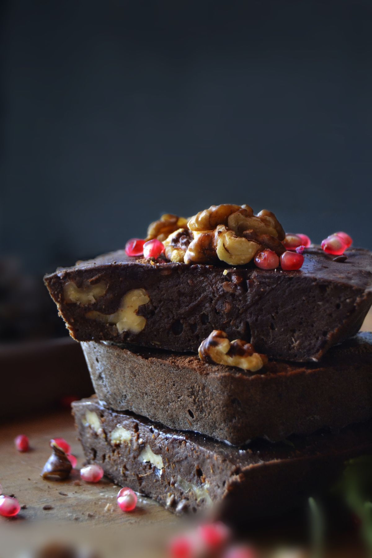 Stack of dark chocolate walnut brownies garnished with pomegranate seeds on a wooden board