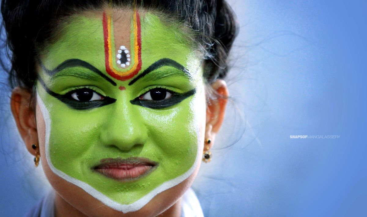 Close portrait of a face painted green with bold black eye makeup and white jawline border