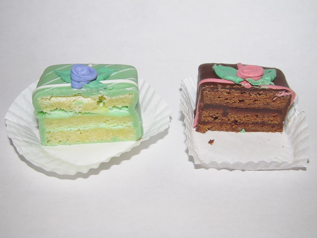Two halved square petit fours with green and chocolate icing and piped frosting roses