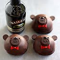 Three dome-shaped chocolate truffles decorated as bear faces with red bowties beside a Baileys bottle