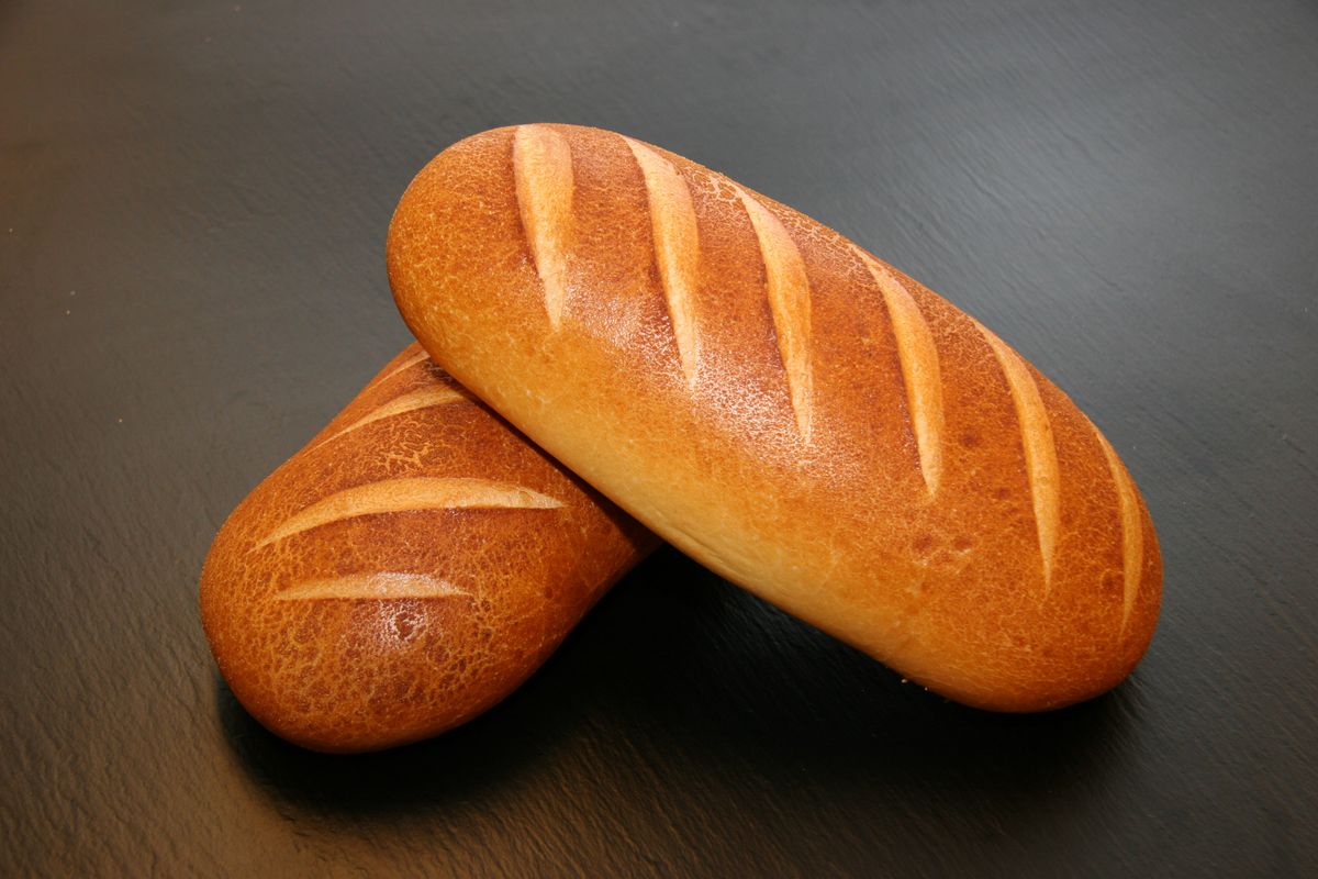 Two small golden-brown oblong loaves with diagonal slashes on a dark slate surface