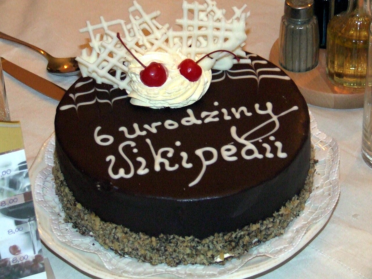 Round chocolate-glazed cake with white cream, cherries, white chocolate lattice, and nut border