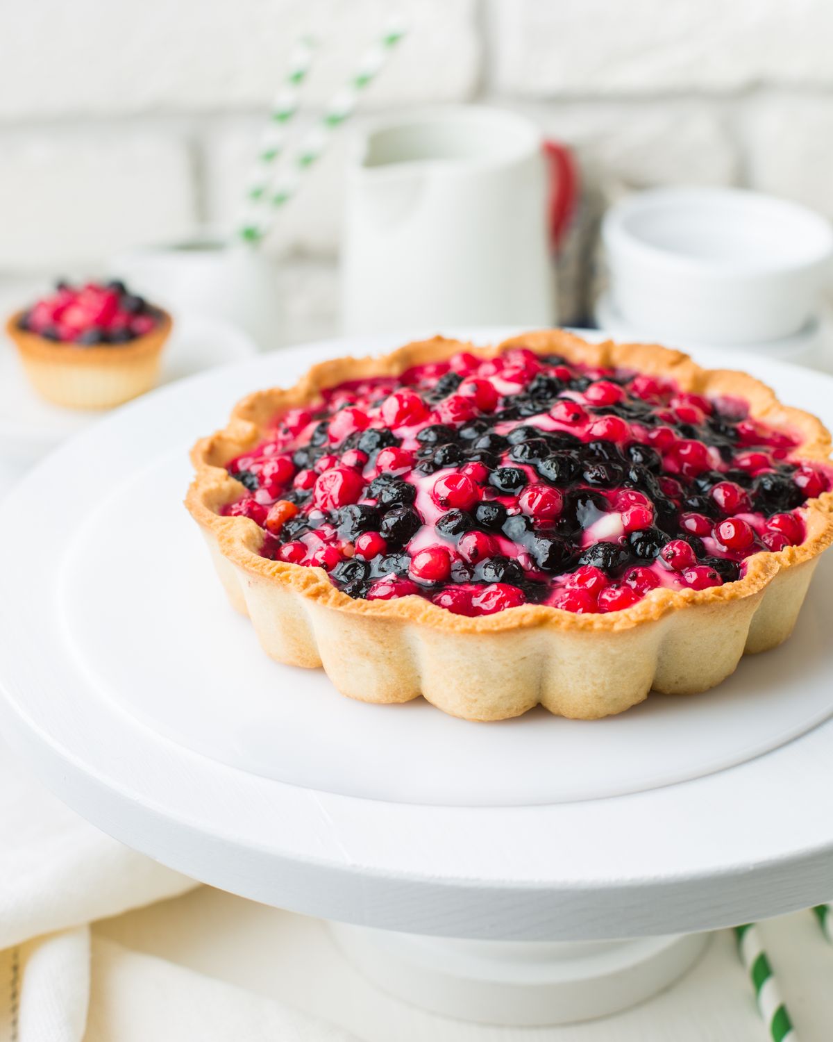 Large berry tart topped with red currants and blueberries on a white cake stand