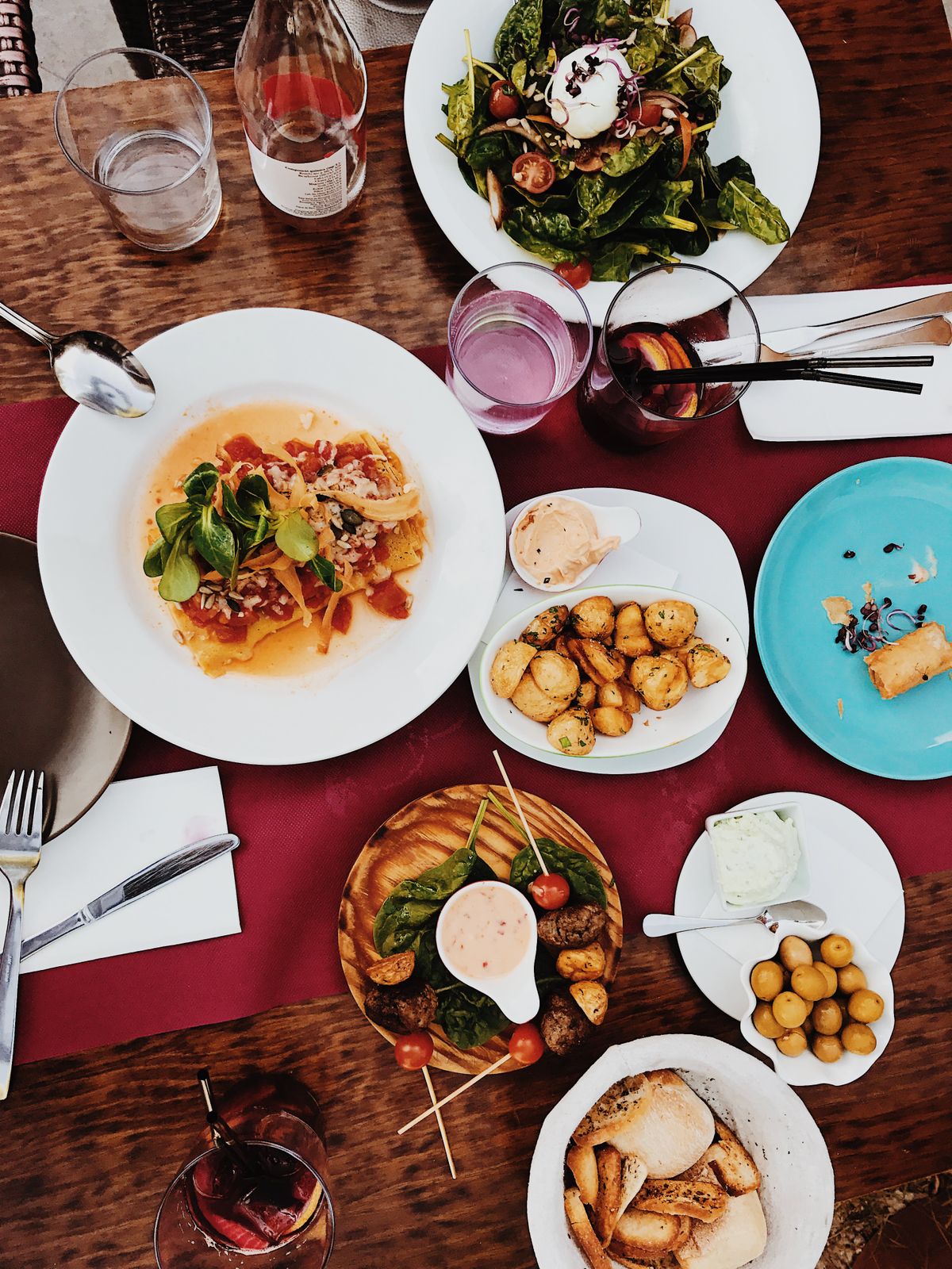 Overhead spread of Mediterranean dishes, roasted potatoes, skewers, and sangria on a wooden table