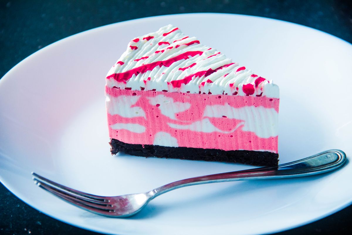 Slice of pink and white swirled mousse cake with chocolate crust and fuchsia drizzle