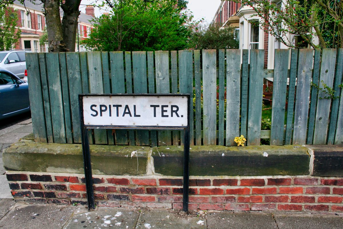 White street sign reading Spital Ter in front of a green fence and brick houses