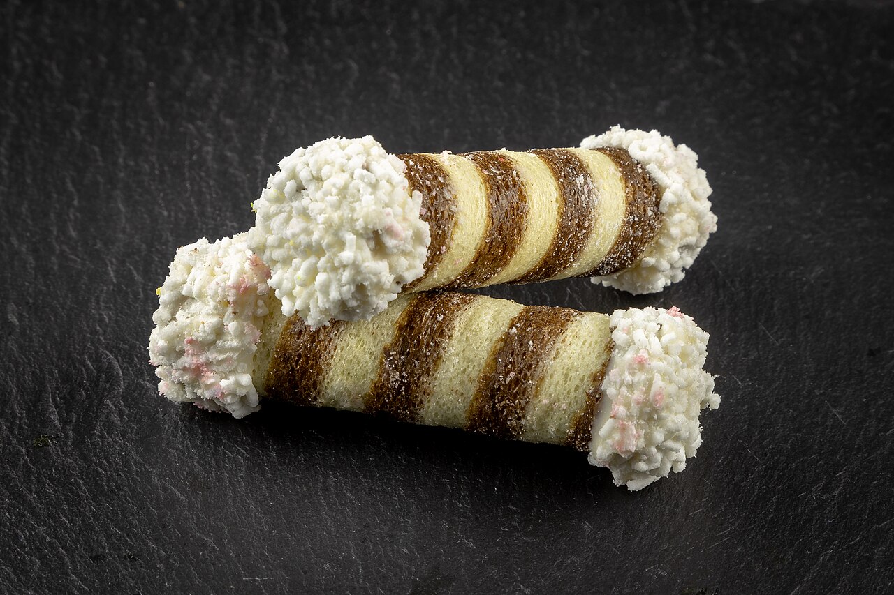 Two rolled tan-and-chocolate striped wafer cookies with white-dipped ends on dark slate