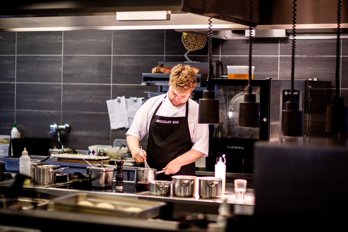 Chef in a white coat whisking a saucepan on a stainless steel kitchen counter