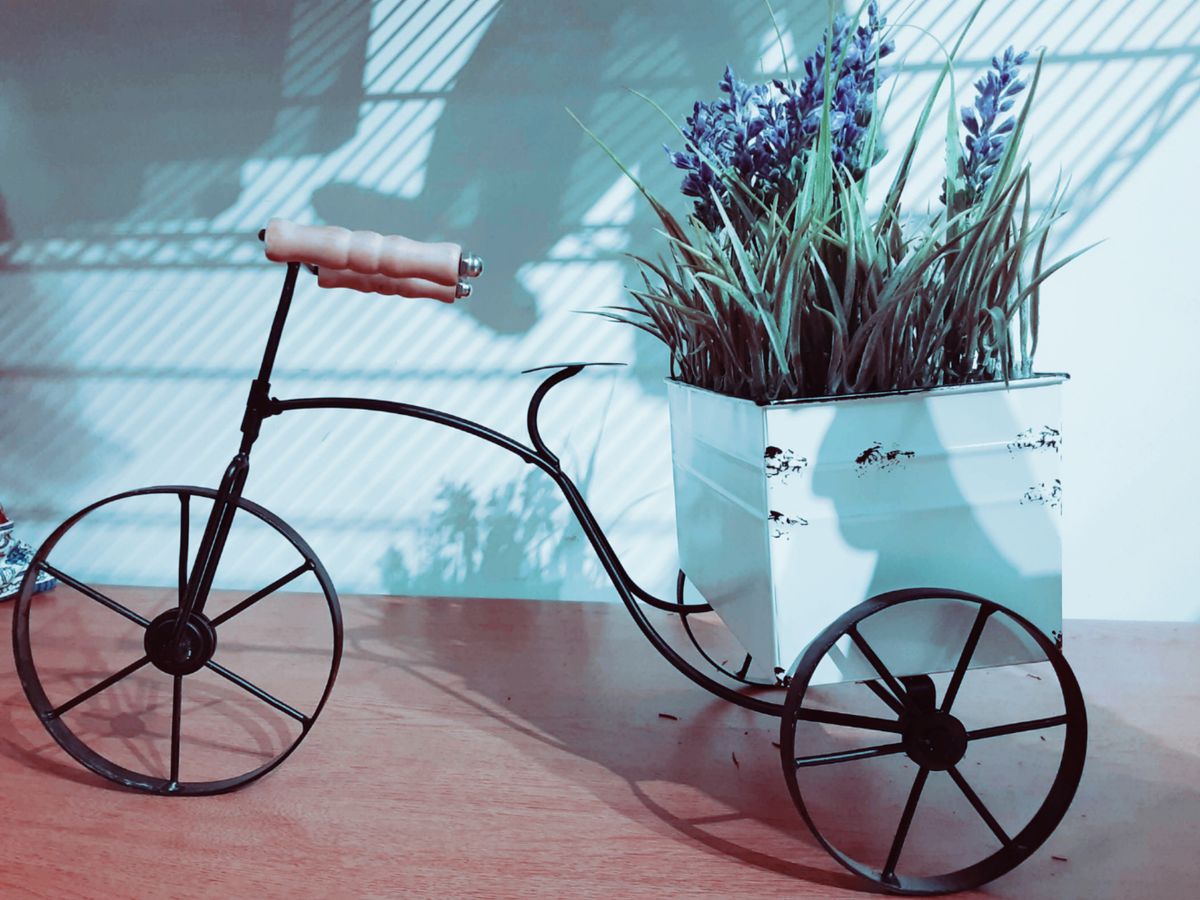 Black wire tricycle planter holding artificial lavender and green grass on a wooden surface