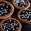 Four mini tarts with golden crusts, dark glossy filling, and white icing constellation star patterns