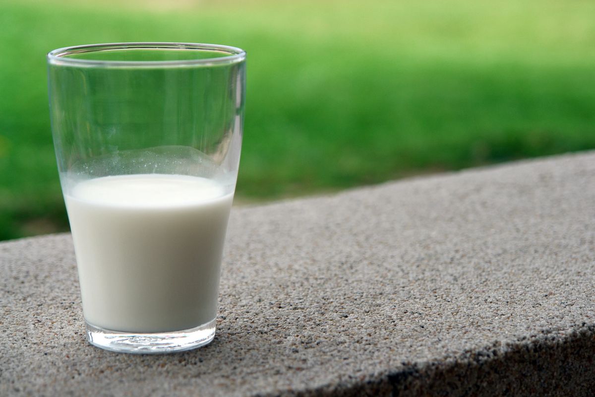 Clear tapered glass half filled with white milk on a stone ledge outdoors
