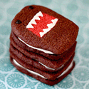 Stack of four Domo-faced chocolate sandwich cookies with white cream and a red mouth with white teeth