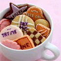 White teacup filled with small pink, orange, and tan cookies piped with Eat Me and Try Me icing