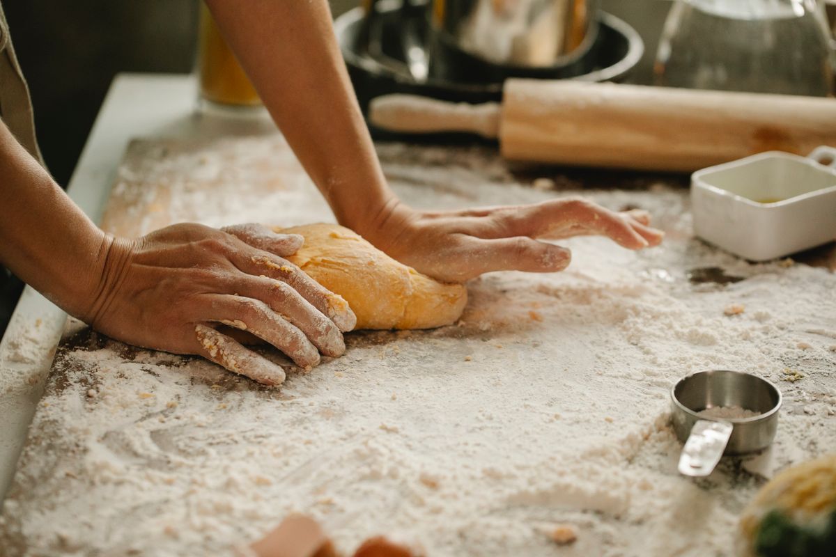 Flour-dusted hands kneading yellow dough on a wooden table with a rolling pin