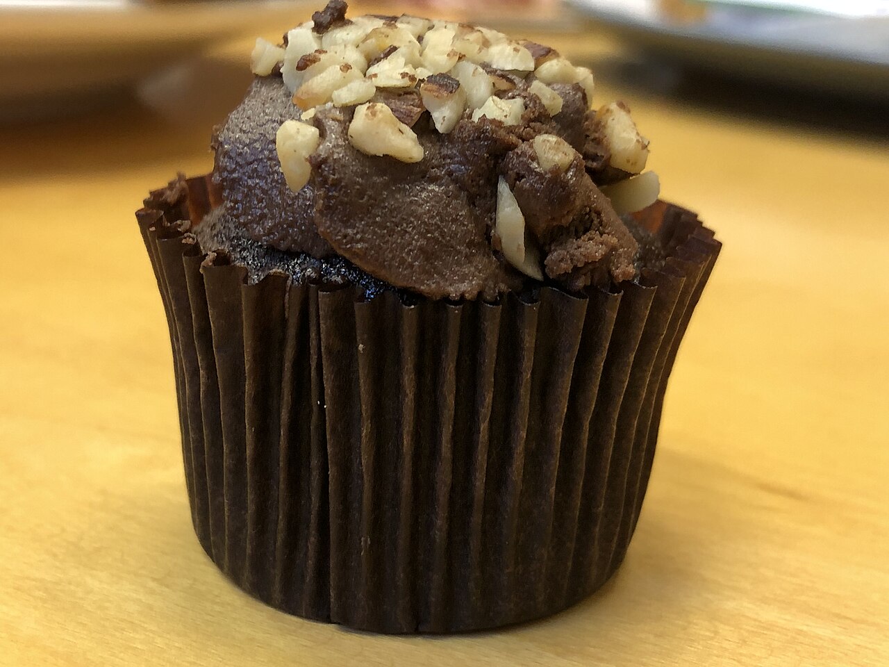 Mini chocolate cupcake in a brown liner topped with dark frosting and chopped nuts