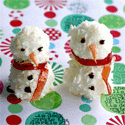 Two coconut snowmen with black-dot eyes and buttons, orange noses, and red-orange scarves on a colorful patterned surface