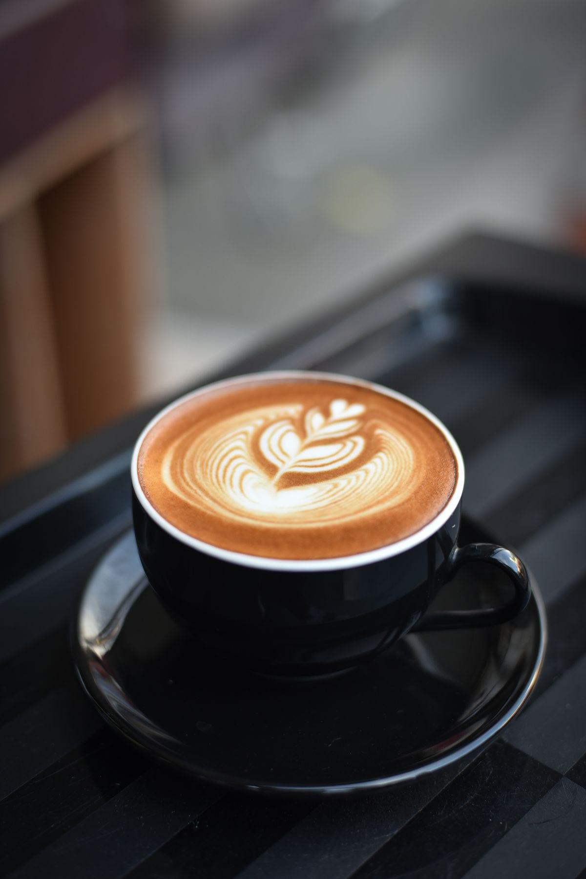 Black cup of latte with white rosetta foam art on a black saucer