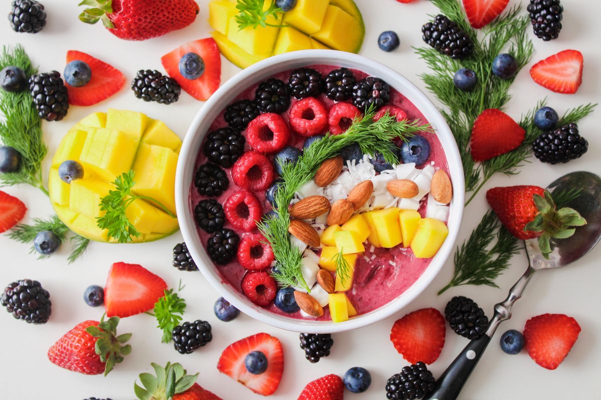 Pink smoothie bowl topped with blackberries, raspberries, blueberries, almonds, coconut, mango, and dill