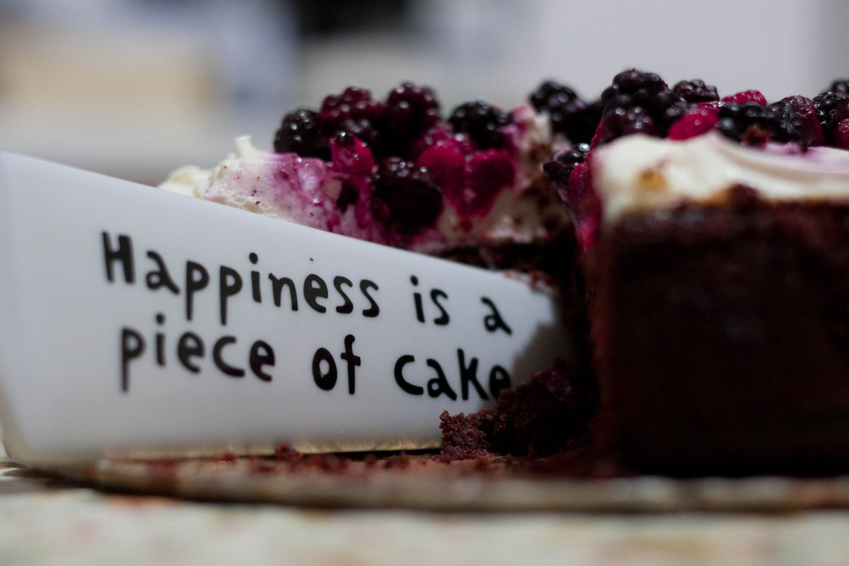 White cake server lifting a slice of dark berry-topped cake from a gold platter