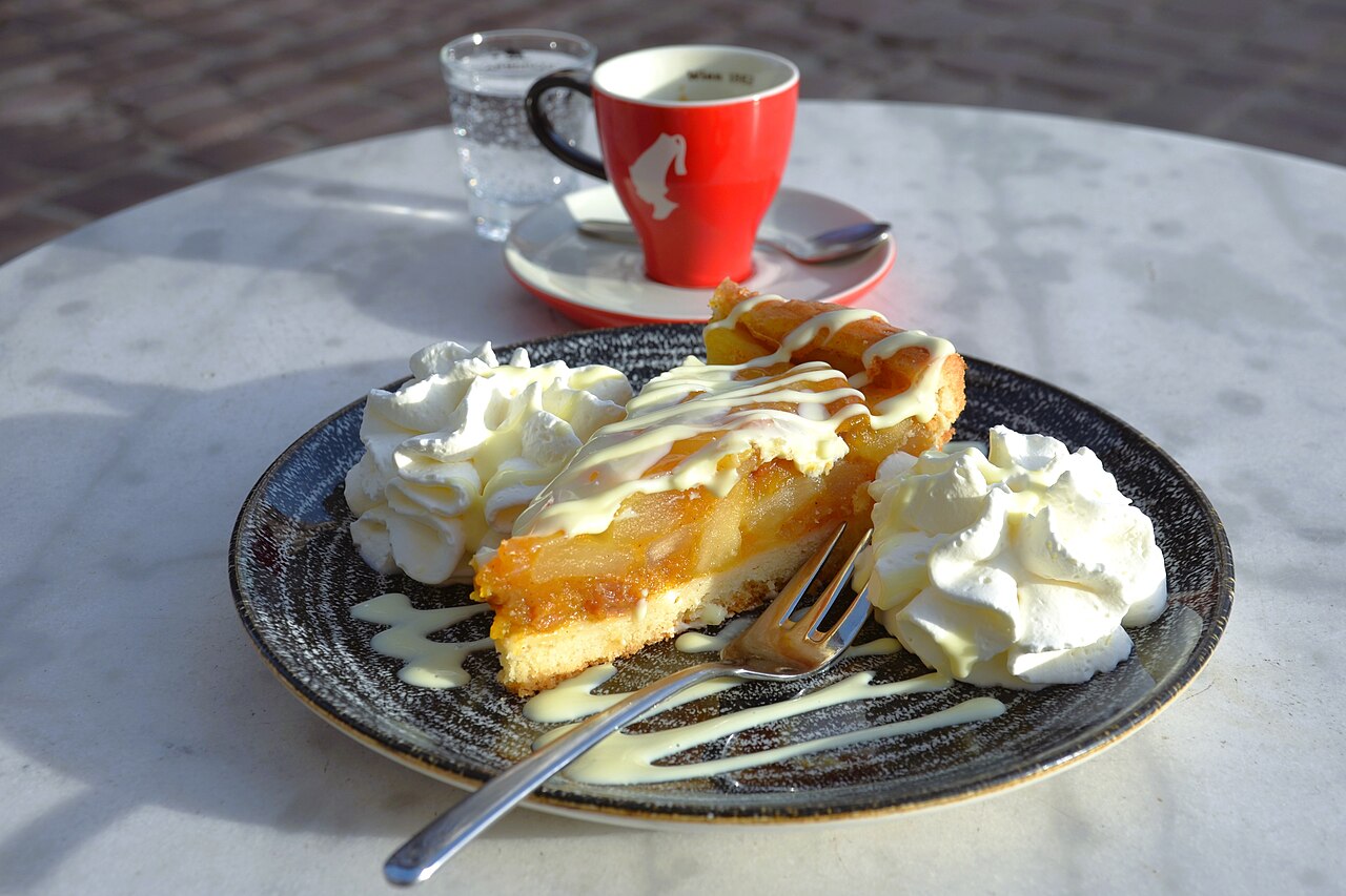 Slice of fruit tart with pale sauce and whipped cream on a dark plate