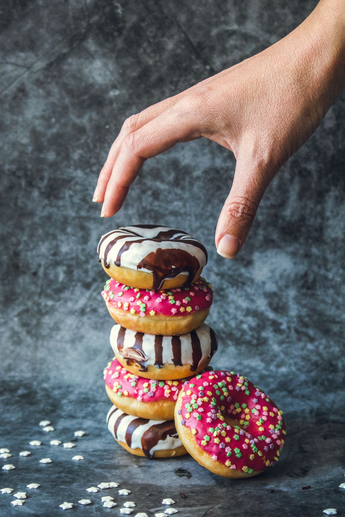 Stack of pink and white frosted donuts with star sprinkles, a hand reaching toward the top