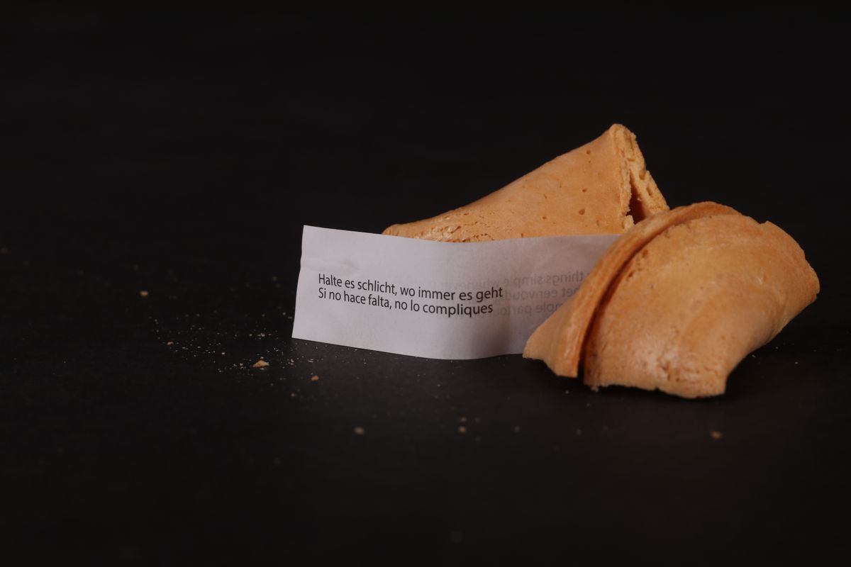 Broken golden fortune cookie showing a multilingual fortune slip on a black surface