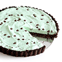 Round mint-green tart with dark chocolate fluted crust and chocolate chips, one slice removed