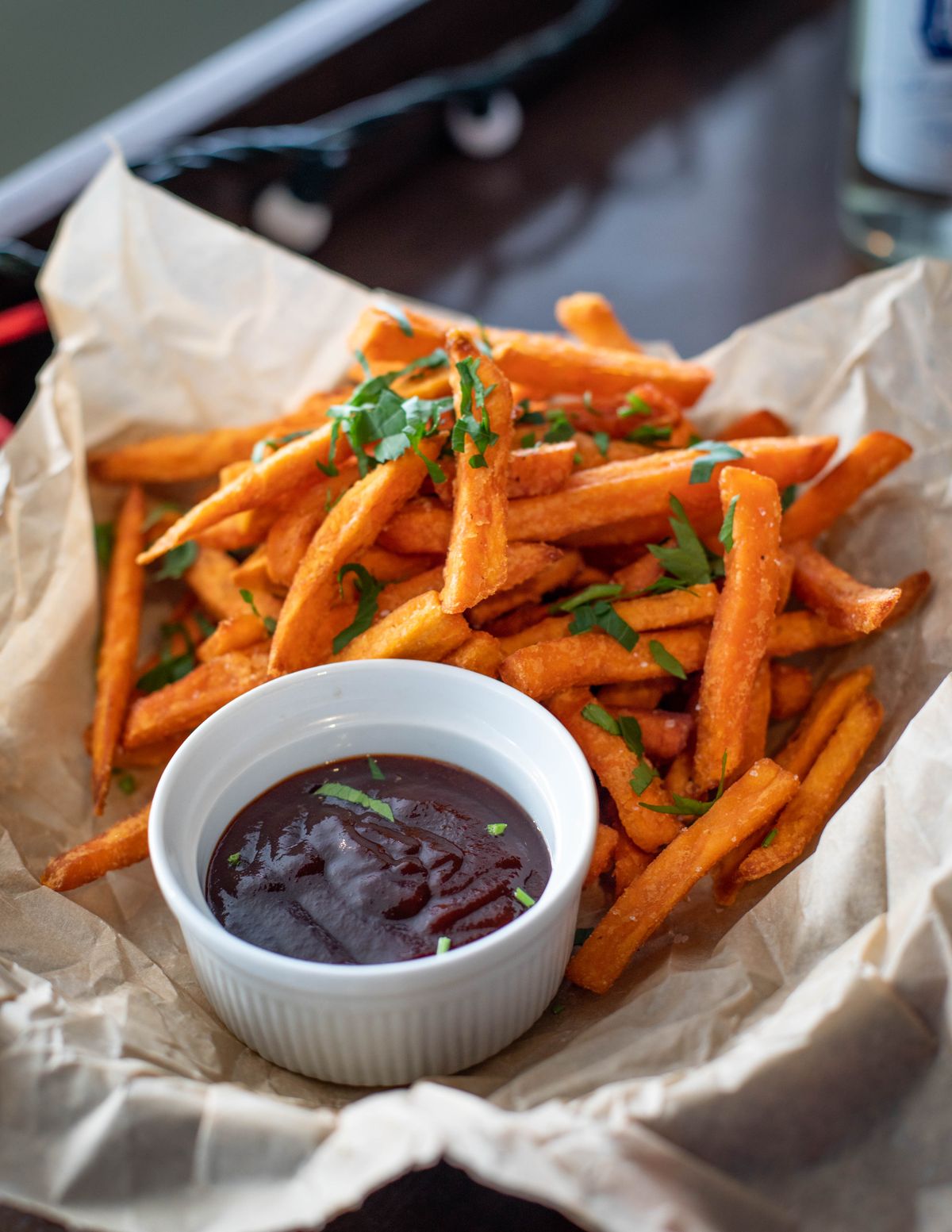 Orange sweet potato fries with parsley beside a small ramekin of dark barbecue sauce