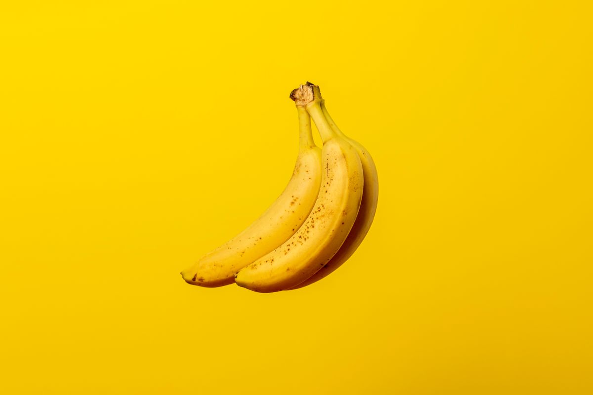 Three ripe yellow bananas with brown speckles on a solid yellow background