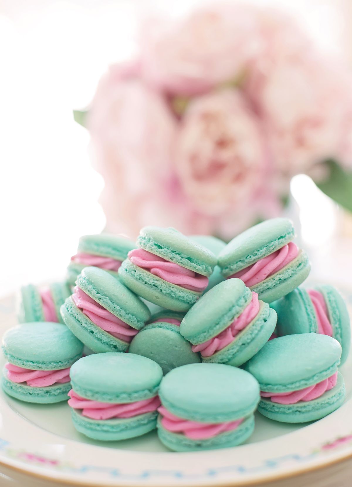 Pile of turquoise macarons with bright pink filling on a floral-rimmed white plate
