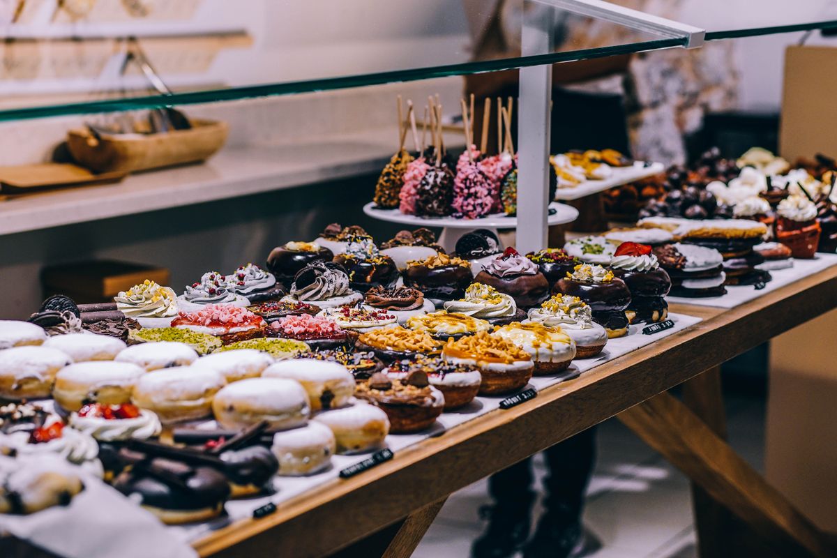 Bakery counter display of assorted glazed donuts, cream-topped pastries, and cake pops