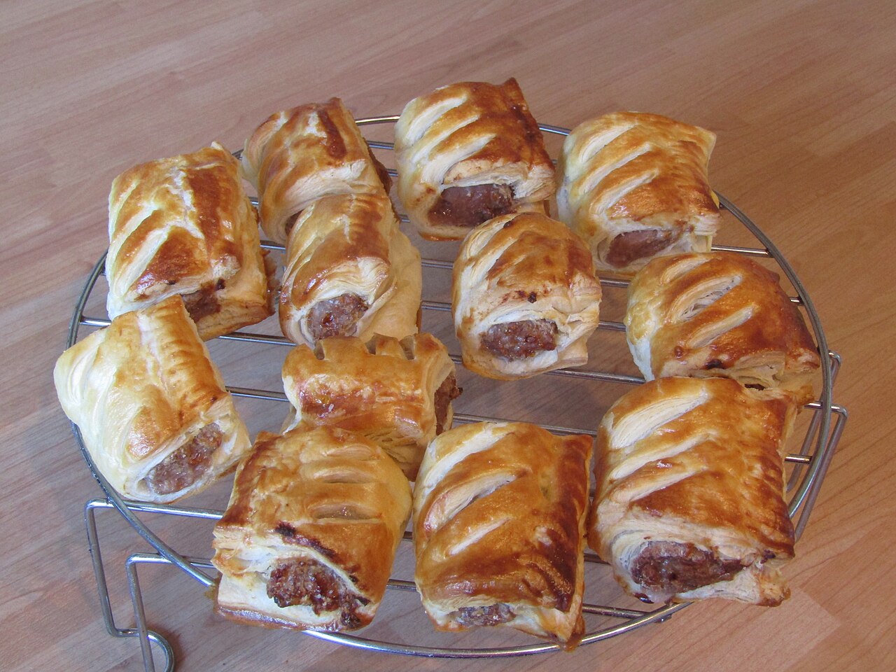 Golden-brown flaky sausage rolls cooling on a round silver wire rack