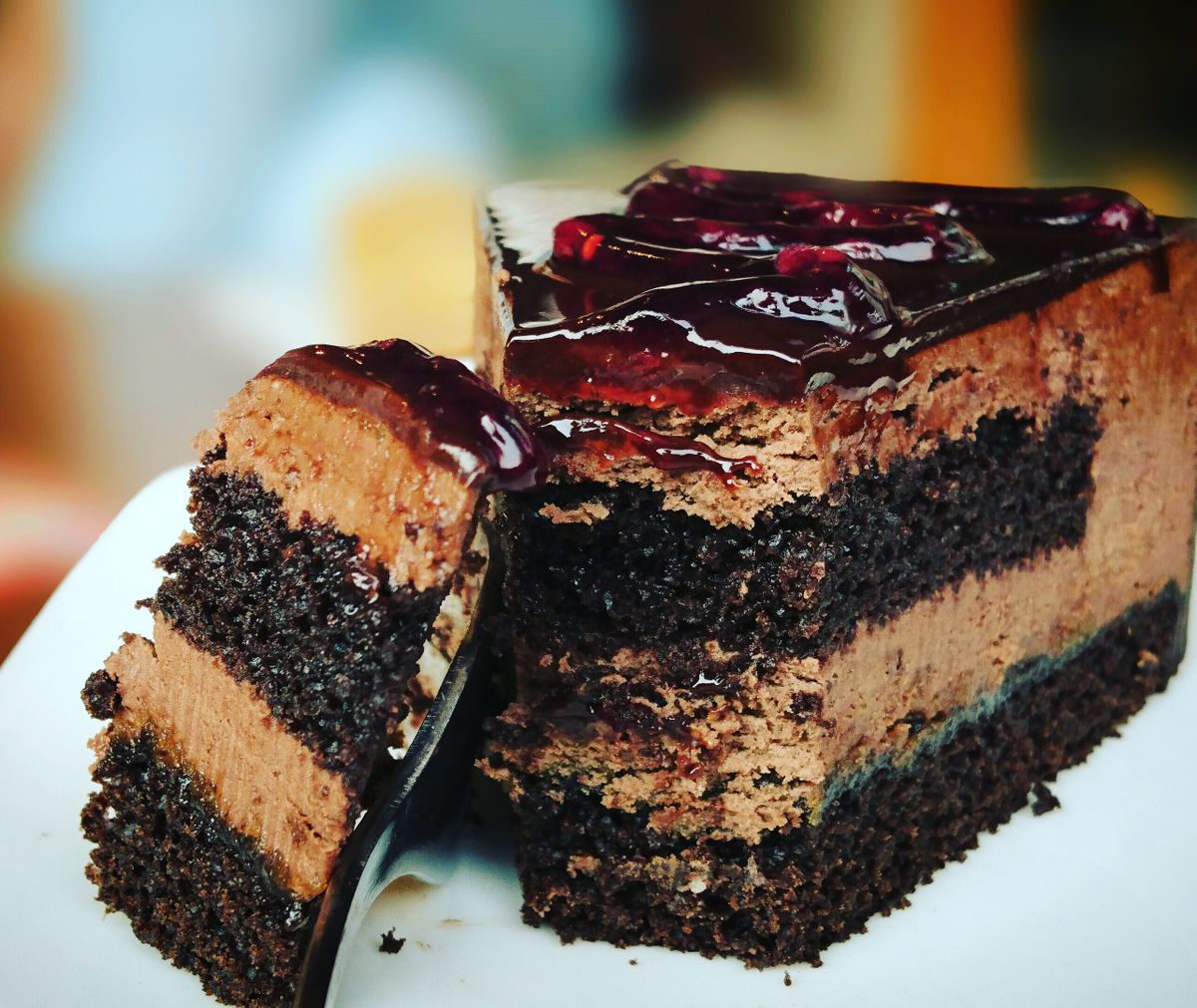 Slice of layered chocolate mousse cake with glossy red berry glaze and a small cut piece on a white plate