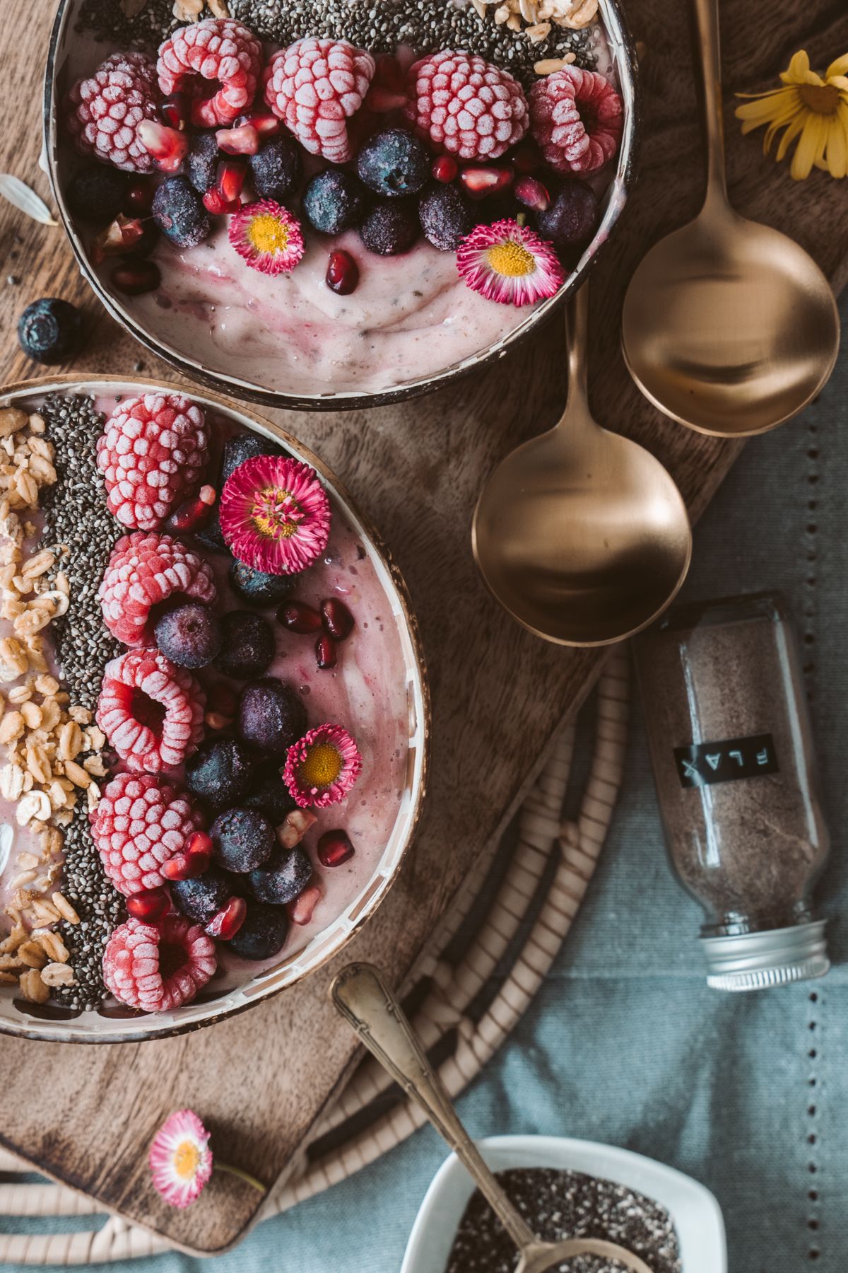 Two pink smoothie bowls topped with frozen berries, granola, and chia seeds in coconut shell bowls