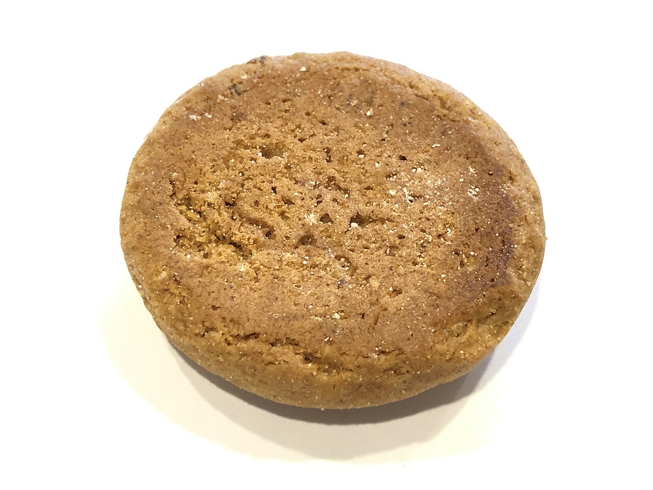 Single thick round golden-brown cookie with a craggy textured surface on a white background