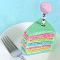 Tall cake slice with pink, yellow, and blue layers, pale green frosting, and a fuzzy pink tree topper