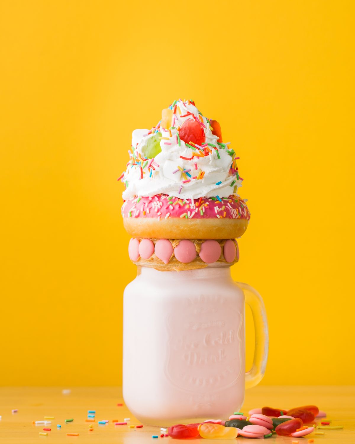 Pink milkshake in a mason jar topped with a frosted donut and whipped cream