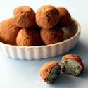 Cocoa-dusted round truffles in a white dish, one halved showing mint-green interior with chocolate chips
