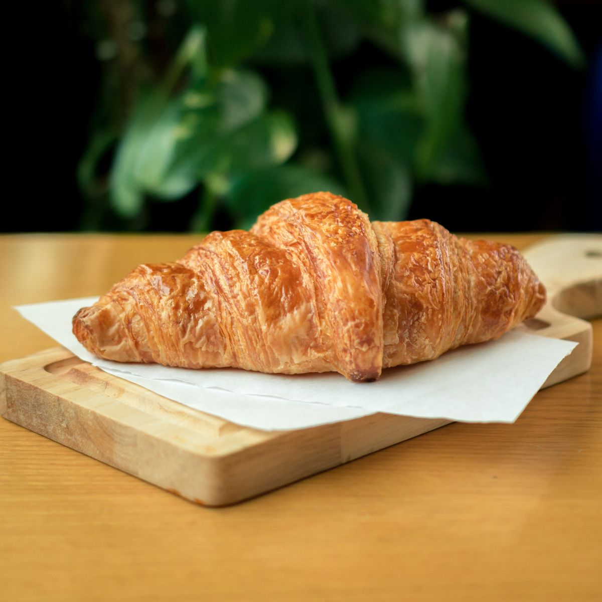 Golden flaky croissant on white parchment atop a small wooden cutting board