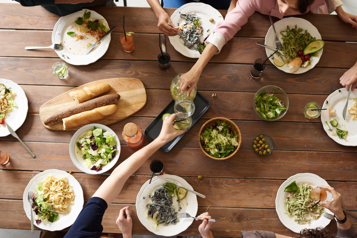 Shared meal with pasta, salad, and baguettes on a rustic wooden table