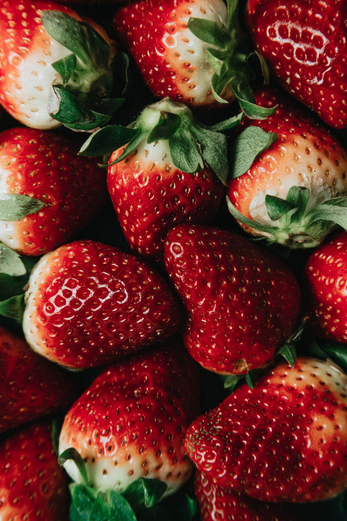 Tight close-up of ripe red strawberries packed together with green hulls attached