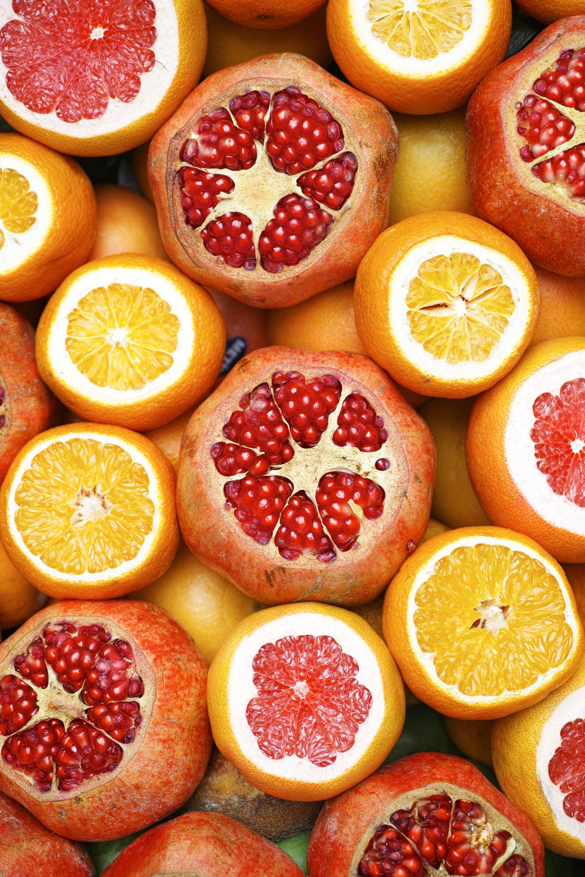 Top-down view of halved pomegranates, oranges, grapefruits, and lemons packed together