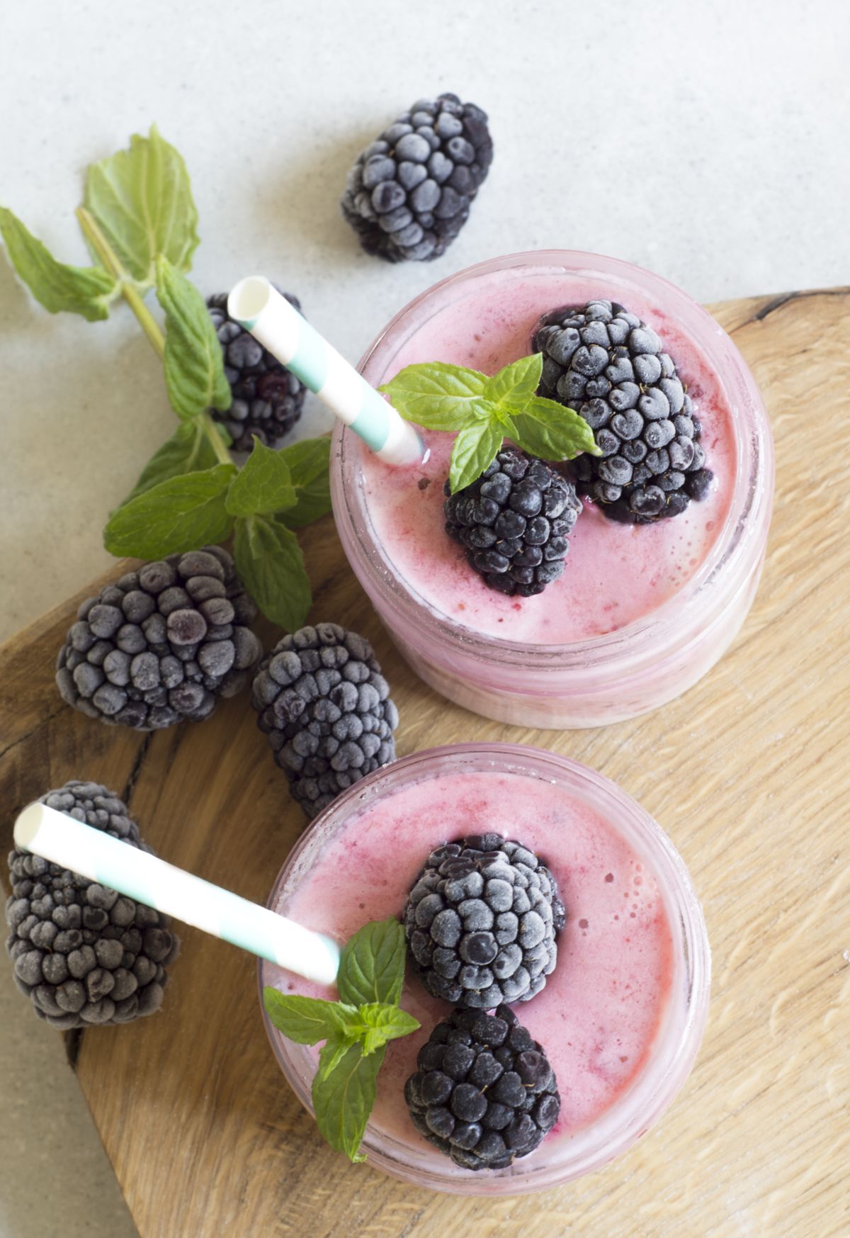 Two jars of pink smoothie topped with frosted blackberries, mint, and striped straws