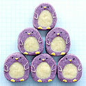 Six purple penguin cookies with cream bellies and yellow beaks and feet stacked on blue grid paper