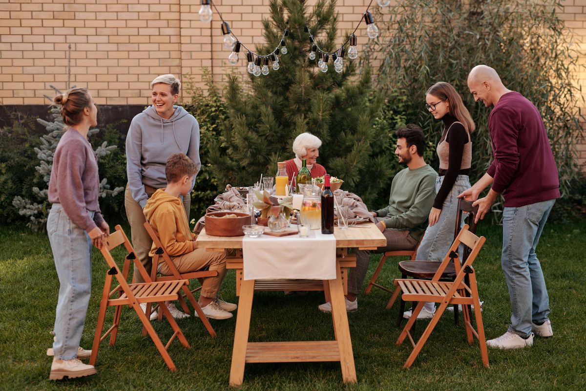 Multi-generational family seated at an outdoor wooden table with wine, bread, and salad