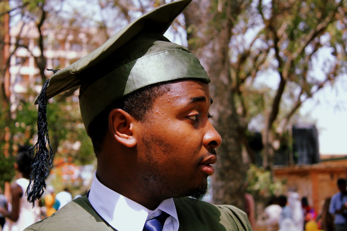 Young man in green graduation cap and gown outdoors at a ceremony