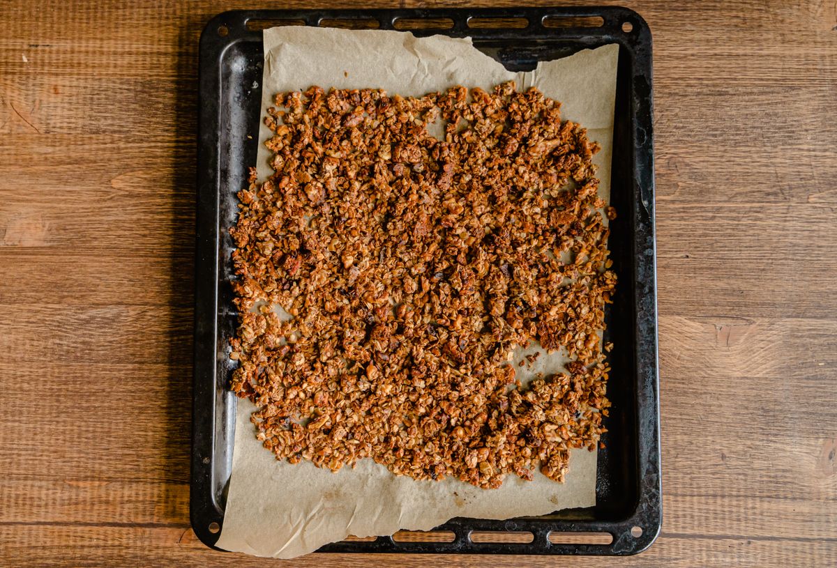 Golden-brown toasted granola clusters spread on parchment in a dark baking tray