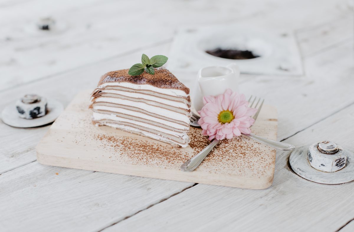 Slice of layered mille crêpe cake dusted with cocoa powder on a small wooden board
