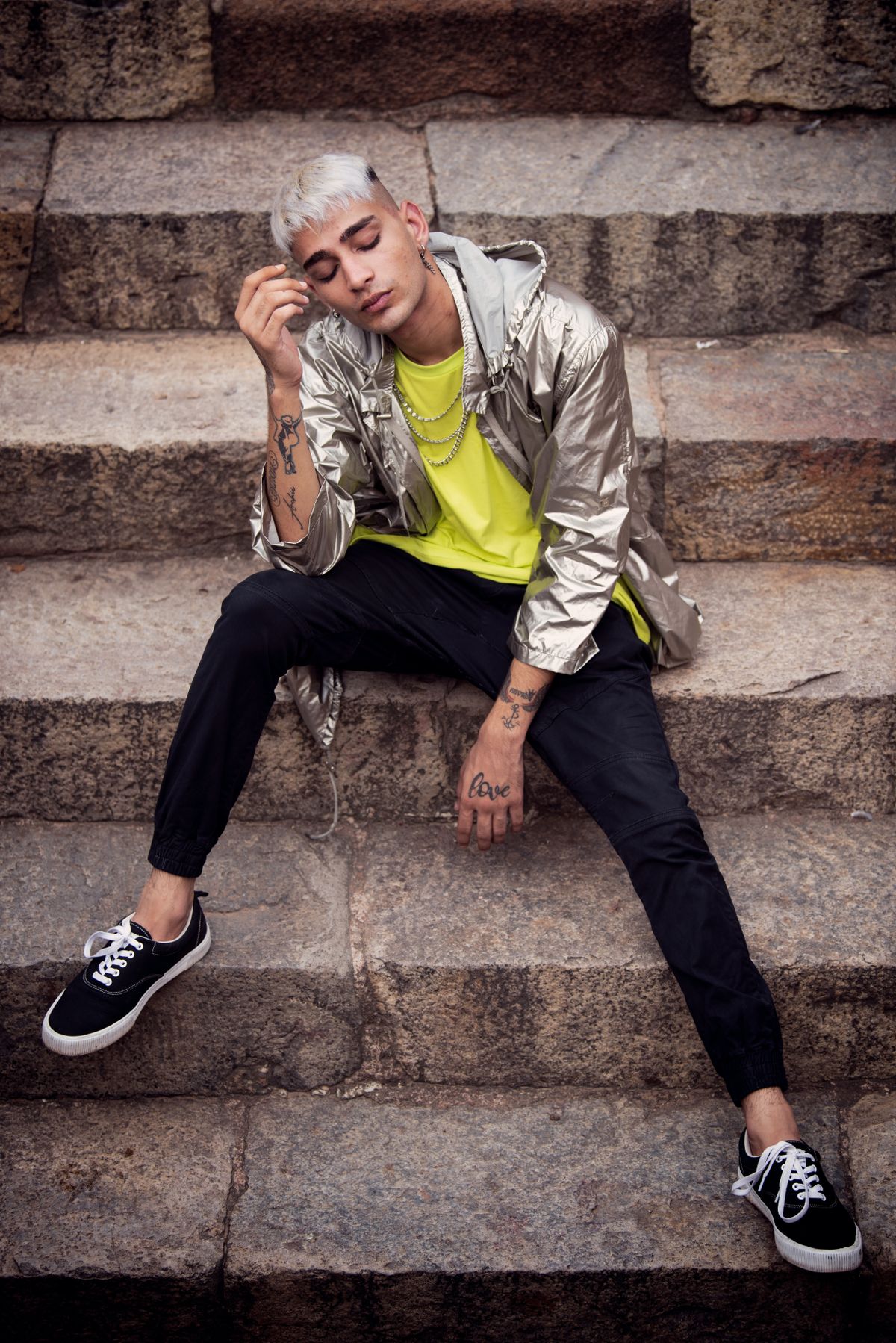 Young man in a silver hooded jacket sitting on weathered stone steps outdoors