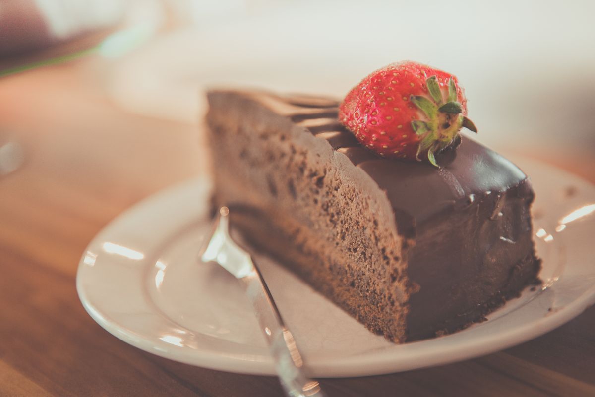 Triangular slice of dark chocolate ganache cake topped with a fresh strawberry on a white plate